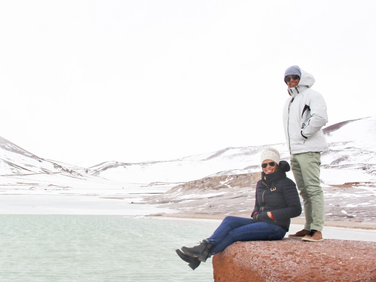 A couple beside a turquoise lagoon in the snow-dusted Atacama in winter